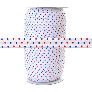 May include: A spool of white elastic with red and blue polka dots. The elastic is wound around a white cardboard spool.