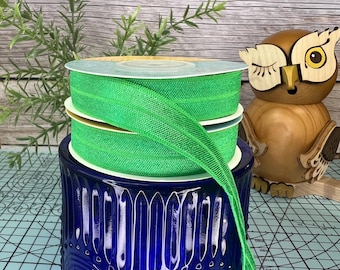May include: A stack of bright green elastic ribbon with a shimmery finish. The ribbon is wound around a blue glass jar with a decorative pattern.