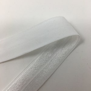 K&ouml;nnte beinhalten: Wei&szlig;er elastischer Besatz mit einer strukturierten Oberfl&auml;che. Der Besatz ist in der Mitte gefaltet, so dass die Innenseite und Au&szlig;enseite des Stoffes sichtbar sind.