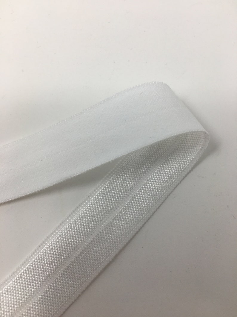 K&ouml;nnte beinhalten: Wei&szlig;er elastischer Besatz mit einer strukturierten Oberfl&auml;che. Der Besatz ist in der Mitte gefaltet, so dass die Innenseite und Au&szlig;enseite des Stoffes sichtbar sind.