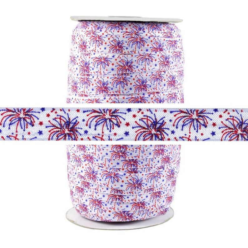 May include: A spool of white elastic with a red and blue firework pattern. The elastic is wound around a cardboard spool.