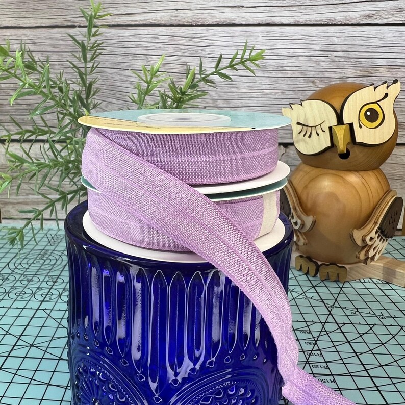 May include: A stack of lilac elastic trim with a blue and white patterned glass jar in the background.