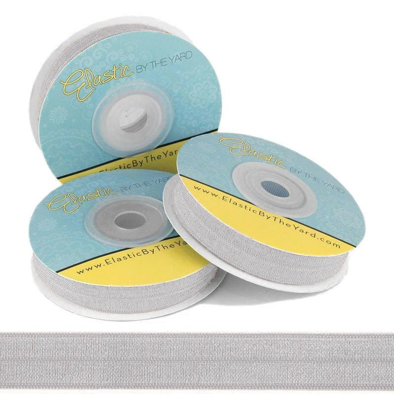 May include: Three spools of silver elastic ribbon with the text "Elastic By The Yard" and the website address "www.ElasticByTheYard.com" printed on the labels.