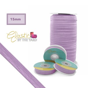 May include: A spool of 15mm wide lavender elastic, with the brand name "Elastic by the Yard" printed on the spool. The elastic is wound around a white cardboard tube.