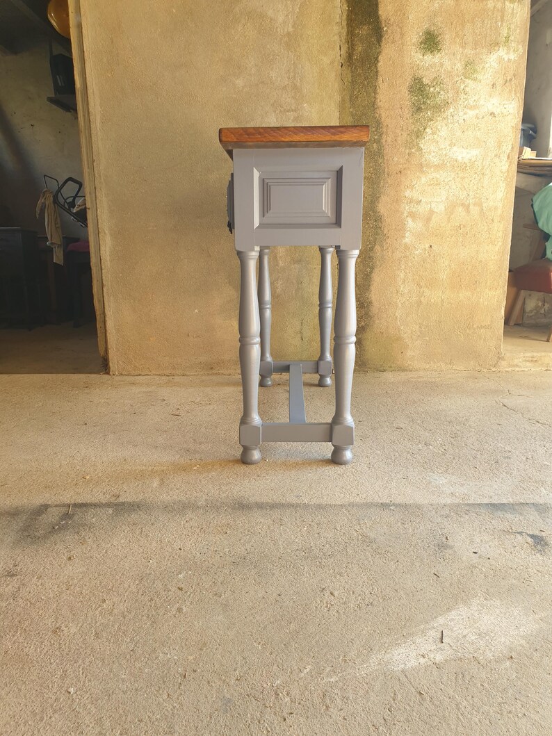 May include: A small, gray painted wooden side table with a dark brown top. The table has four turned legs and a rectangular cabinet door. The table is approximately 30 inches tall.