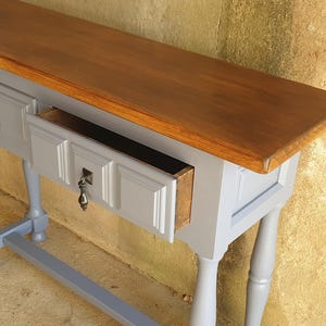 May include: A gray console table with a brown wooden top and two drawers. One drawer is open, revealing the interior. The table has ornate legs and drawer pulls.