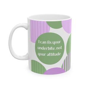 Puede incluir: Taza de cerámica blanca con asa curva. La taza presenta un diseño de círculos y rayas verdes y moradas. El texto de la taza dice: "I can fix your underbite, not your attitude."
