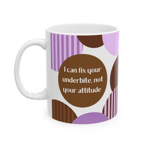 Puede incluir: Taza de cerámica blanca con asa, con un diseño de círculos y rayas moradas y marrones. La taza tiene el texto "I can fix your underbite, not your attitude" en un círculo marrón.
