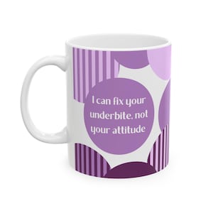 Puede incluir: Taza de cerámica blanca con asa curva. La taza presenta un diseño de círculos morados y rayas verticales. El texto "I can fix your underbite, not your attitude" está impreso en la taza en un círculo morado.