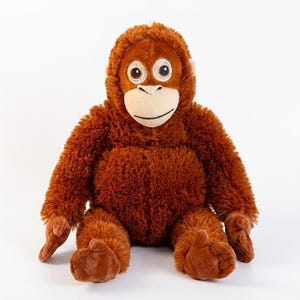 May include: A plush orangutan toy with brown fur, a tan face, and large, round eyes. The stuffed animal has a friendly expression and is sitting upright. The toy is designed to resemble a real orangutan.