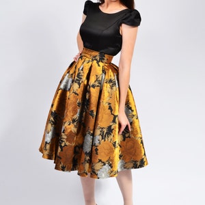 May include: A woman wearing a black top and a gold and black floral skirt. She is wearing gold heels.