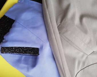May include: Two pieces of fabric, one light blue and one gray, are shown side by side. The light blue fabric has a black sparkly trim on the edge. The gray fabric has a single pocket.