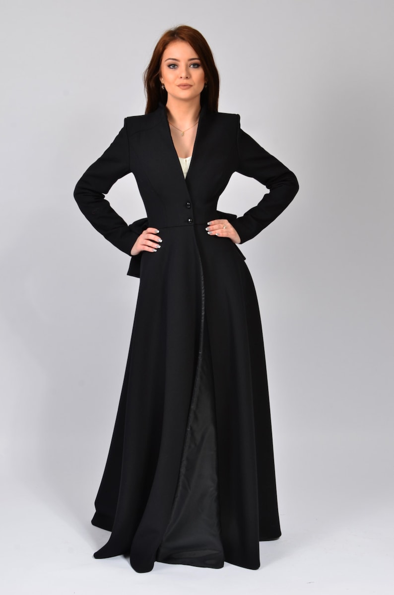 May include: A long black coat with a fitted waist and a flowing skirt. The coat has a V-neckline and a single button closure at the waist.