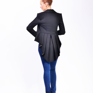 May include: A black blazer with a long, flowing back panel. The blazer is worn over blue jeans and black high heels.