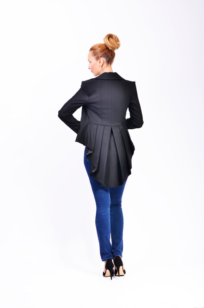 May include: A black blazer with a long, flowing back panel. The blazer is worn over blue jeans and black high heels.