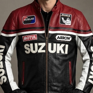 May include: A black, red, and white leather motorcycle jacket with the word "SUZUKI" prominently displayed across the chest. The jacket features patches for "Team SUZUKI", "MICHELIN", "MOTUL", and "ARROW". The sleeves also have the word "SUZUKI" in white.