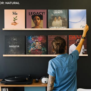 Może przedstawiać: Prezentacja płyt winylowych na drewnianych półkach na tle ciemnej ściany. Płyty zawierają okładki albumów z tekstami, w tym "Ma", "LEGACY!", "Carrie & Lowell", "DAUGHTER" i "Stranger Things". Widoczny jest gramofon i głośniki.