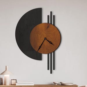 Pode incluir: Um relógio de parede moderno com um semicírculo preto e linhas verticais, e um mostrador redondo de madeira. Os ponteiros do relógio são pretos. O texto "Color: WENGE + BEECH" é visível. O relógio está montado numa parede branca.
