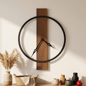 Puede incluir: Un reloj de pared moderno con un marco circular negro y manecillas negras. La esfera del reloj es abierta, con las manecillas montadas en un panel de madera vertical. El reloj está montado en una pared blanca. Una mesa de madera debajo contiene objetos decorativos.