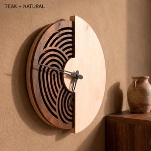 May include: A circular wall clock featuring a split design with a dark brown wood section on the left displaying intricate cut-out concentric arc patterns and a smooth light-coloured wood section on the right. Black metal clock hands are centred.