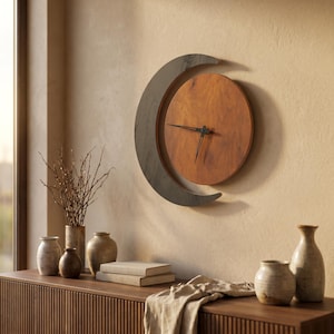 May include: A wall clock featuring a circular wooden face with a warm brown grain, partially enclosed by a dark gray crescent-shaped frame. The clock has two thin black hands positioned at the center of the circular face to indicate the time.