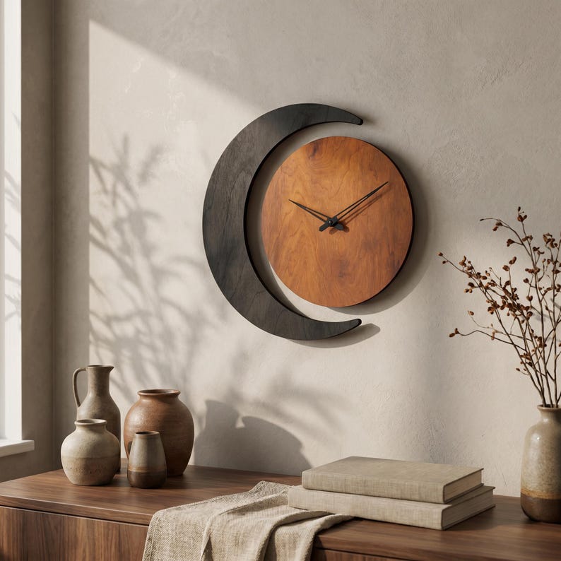 May include: A wall clock featuring a circular wooden face with a warm brown grain pattern, surrounded by a dark charcoal-colored crescent moon frame. The clock has two thin black hands positioned at the center of the circular wooden dial.