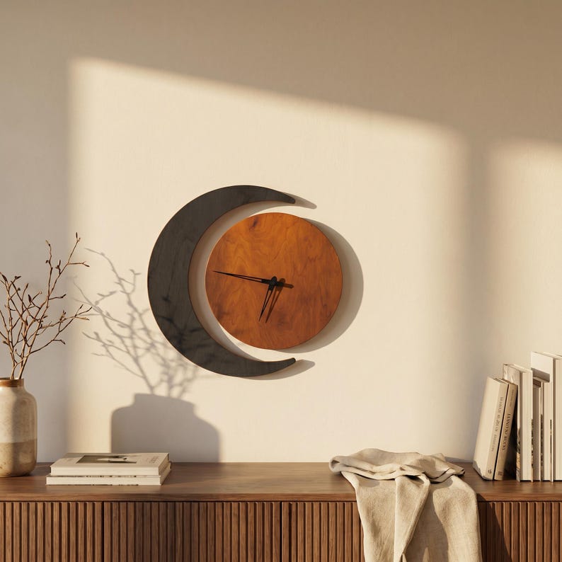May include: A wall clock featuring a circular wooden face with a warm brown grain, partially encircled by a dark, crescent-shaped frame. The clock has thin black hands positioned at the center of the wooden circle, mounted on a plain wall.