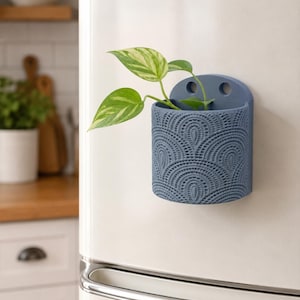 May include: A blue decorative wall planter with a detailed, repeating pattern, holding a small green and white plant. The planter is mounted on a white surface, likely a refrigerator, adding a touch of nature to the kitchen.
