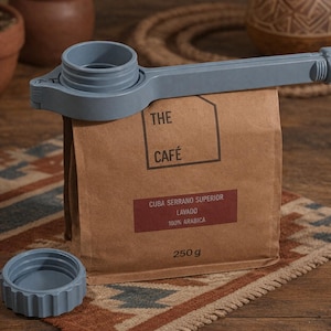 May include: A white ceramic mug with a black handle and the text "But First, Coffee" in a bold, black font. The mug is set against a blurred background, suggesting a cozy setting.