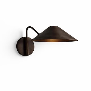 May include: A bronze wall sconce featuring a conical shade and a curved arm. The shade has a warm, golden interior. The sconce is mounted on a circular base. The design is minimalist and modern, suitable for various interior styles.