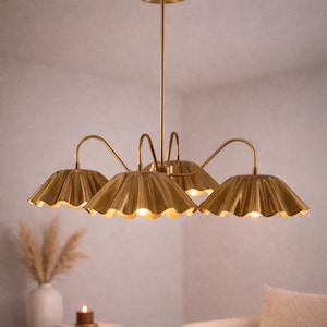 May include: A gold-colored chandelier with four lampshades. Each lampshade has a scalloped edge and a curved arm. The light fixture is suspended from the ceiling by a central rod. The lampshades are lit, casting a warm glow.