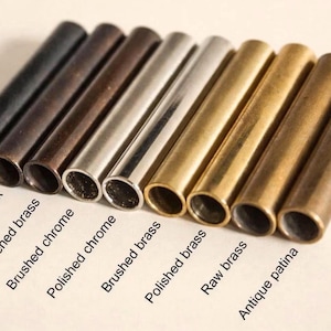 May include: An assortment of metal tubes in various finishes, including matte black, antique black, and polished brass. The image displays a range of colors and textures, with labels identifying each finish. The tubes are cylindrical and appear to be components or decorative elements.