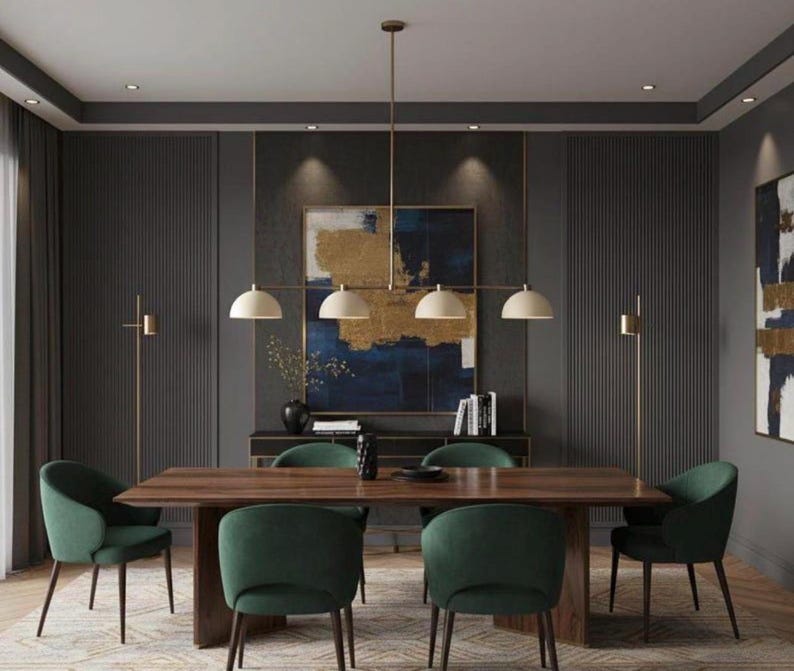 May include: A rectangular wooden dining table with four dark green upholstered chairs, a linear pendant light with four cream-colored dome shades, and two thin floor lamps positioned in a room with dark gray paneled walls and abstract art.
