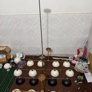 May include: A multi-tiered chandelier featuring a central dark metal rod and horizontal arms. The fixture includes sixteen dome-shaped shades, with twelve in white and four in black, arranged in a grid pattern. Gold-toned accents connect the shades.