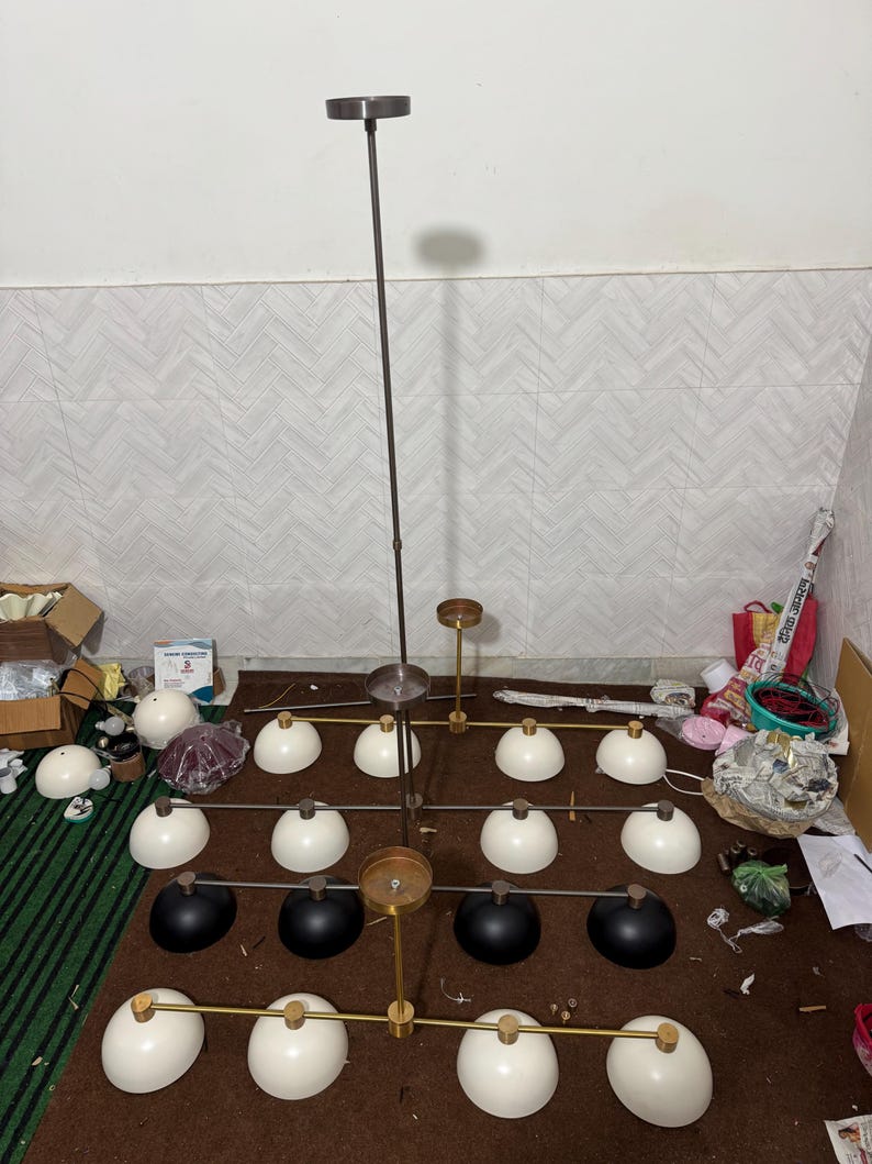 May include: A multi-tiered chandelier featuring a central dark metal rod and horizontal arms. The fixture includes sixteen dome-shaped shades, with twelve in white and four in black, arranged in a grid pattern. Gold-toned accents connect the shades.