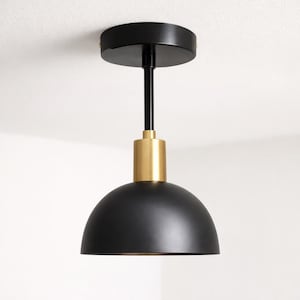 May include: A black and gold pendant light. The light features a black, dome-shaped shade, a gold-coloured cylindrical section, and a black rod connecting to a circular ceiling mount. Designed for ceiling installation.