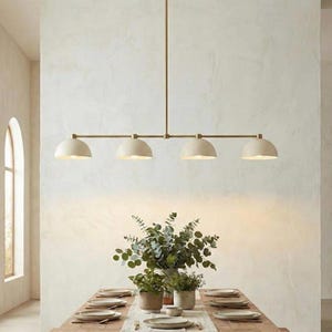 May include: A modern dining room with a long wooden table set for a meal. Above the table hangs a brass light fixture with four cream-colored dome-shaped shades. The room has arched windows and a neutral color palette.