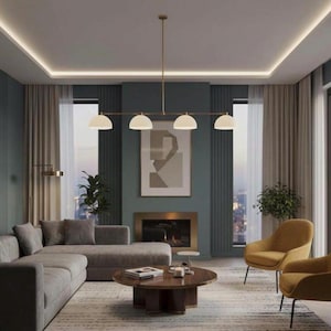 May include: A linear chandelier featuring four white semi-spherical glass shades suspended from a thin gold-toned metal rod. The fixture is centered horizontally, providing downward illumination over a circular wooden coffee table in a living room.
