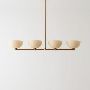 May include: A modern, four-light pendant light fixture. It features four cream-colored, bowl-shaped shades suspended from a bronze-colored metal frame. The fixture is attached to the ceiling by a single bronze-colored rod.