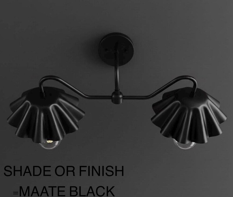 May include: Matte black two-light wall sconce. The fixture features two ruffled shades and a curved arm design. The text at the bottom of the image reads "SHADE OR FINISH = MAATE BLACK".