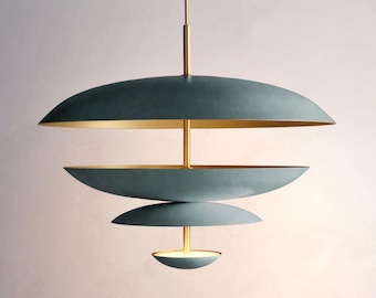 May include: A modern, tiered pendant light fixture. The fixture features three teal-colored, saucer-shaped shades with gold-colored interiors. A central gold-colored rod supports the shades, and a single light source is visible at the bottom.