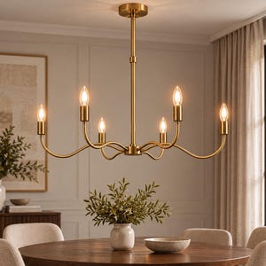 May include: A six-light chandelier with a brushed brass finish, featuring curved arms extending from a central vertical rod. The fixture includes six upright candle-style light sockets, each holding a glowing bulb, suspended from a circular ceiling canopy.