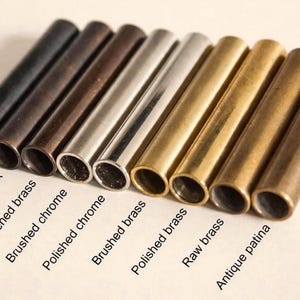 May include: An assortment of metal tubes in various finishes, including matte black, antique black, and polished brass. The image displays a range of colors and textures, with labels identifying each finish. The tubes are cylindrical and appear to be components or decorative elements.