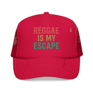 May include: A red trucker hat with the text "REGGAE IS MY ESCAPE" in gold, green, and brown. The hat has a mesh back and a curved brim. A small gold emblem is on the right side.