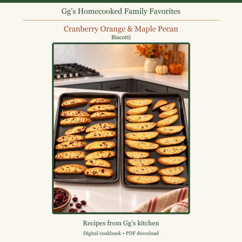 May include: A digital cookbook titled Gg's Homecooked Family Favorites featuring a recipe for Cranberry Orange & Maple Pecan Biscotti. The image displays two black baking sheets filled with rows of golden-brown biscotti on a white counter.