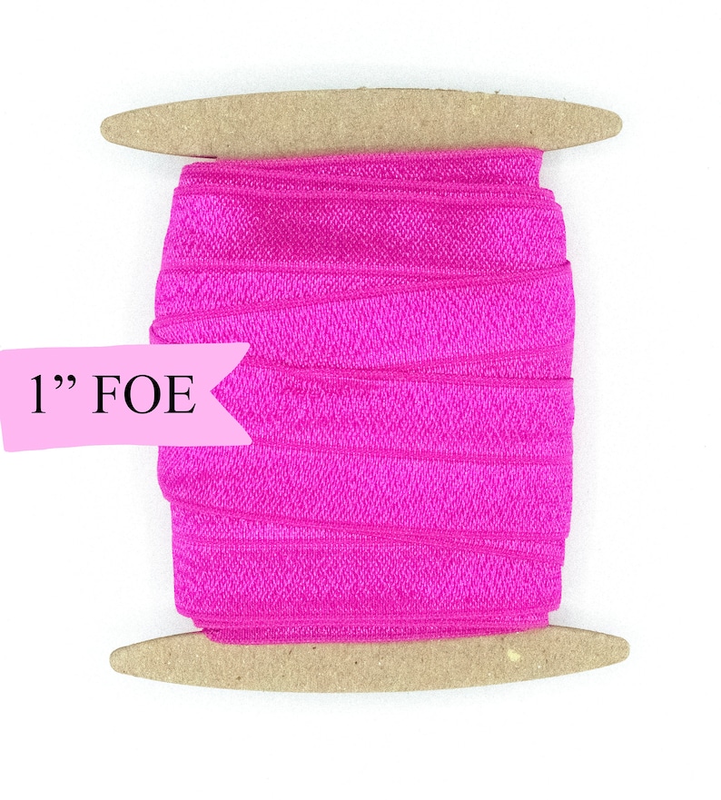 May include: A spool of 1" wide pink fold over elastic (FOE) on a wooden dowel.