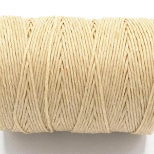 Puede incluir: Un carrete de hilo de color natural. El hilo est&aacute; enrollado firmemente, creando una forma cil&iacute;ndrica. El color es beige claro y la textura parece ligeramente &aacute;spera. Este hilo es adecuado para manualidades, envolver regalos y varios proyectos de bricolaje.