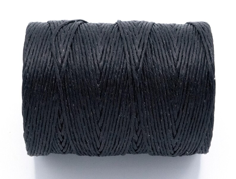 Puede incluir: Un carrete de hilo negro, enrollado con fuerza. El hilo es de un material texturizado y est&aacute; dispuesto en un patr&oacute;n entrecruzado. El fondo es blanco liso. Ideal para manualidades.