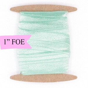 May include: A spool of 1" wide light green folded over elastic (FOE) ribbon. The ribbon is wound around a brown cardboard spool.