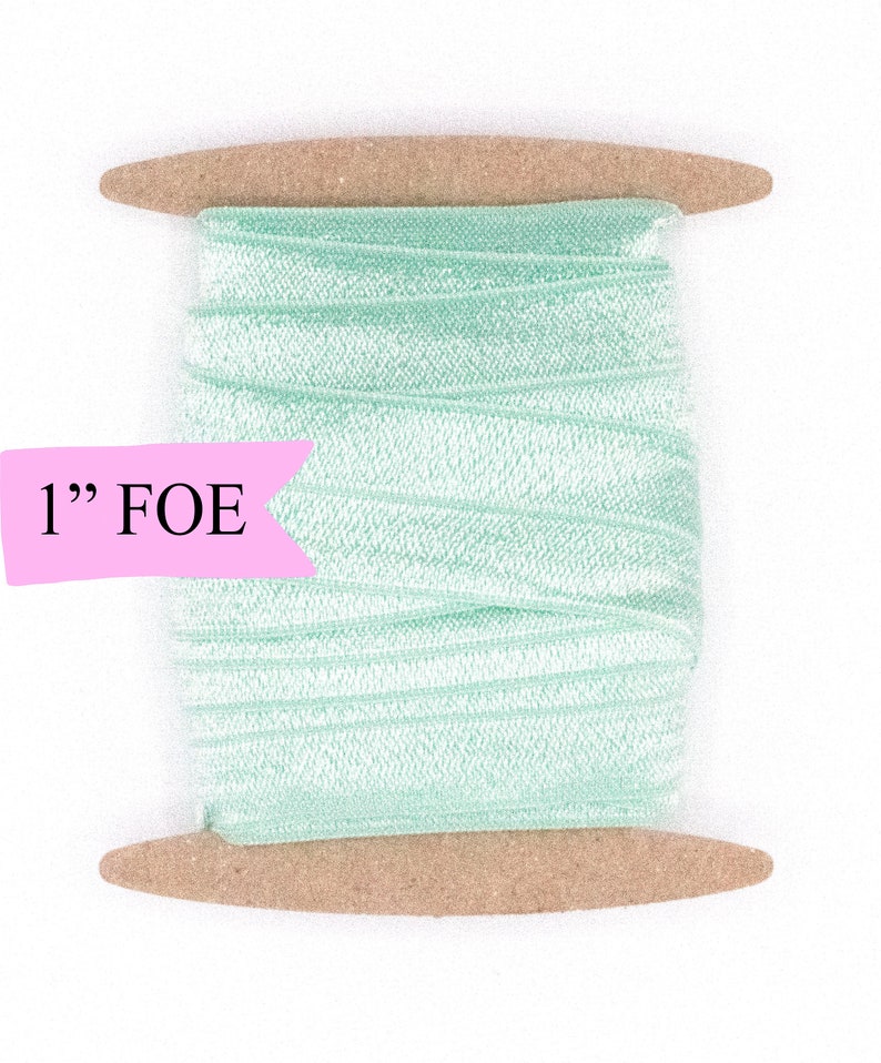 May include: A spool of 1" wide light green folded over elastic (FOE) ribbon. The ribbon is wound around a brown cardboard spool.